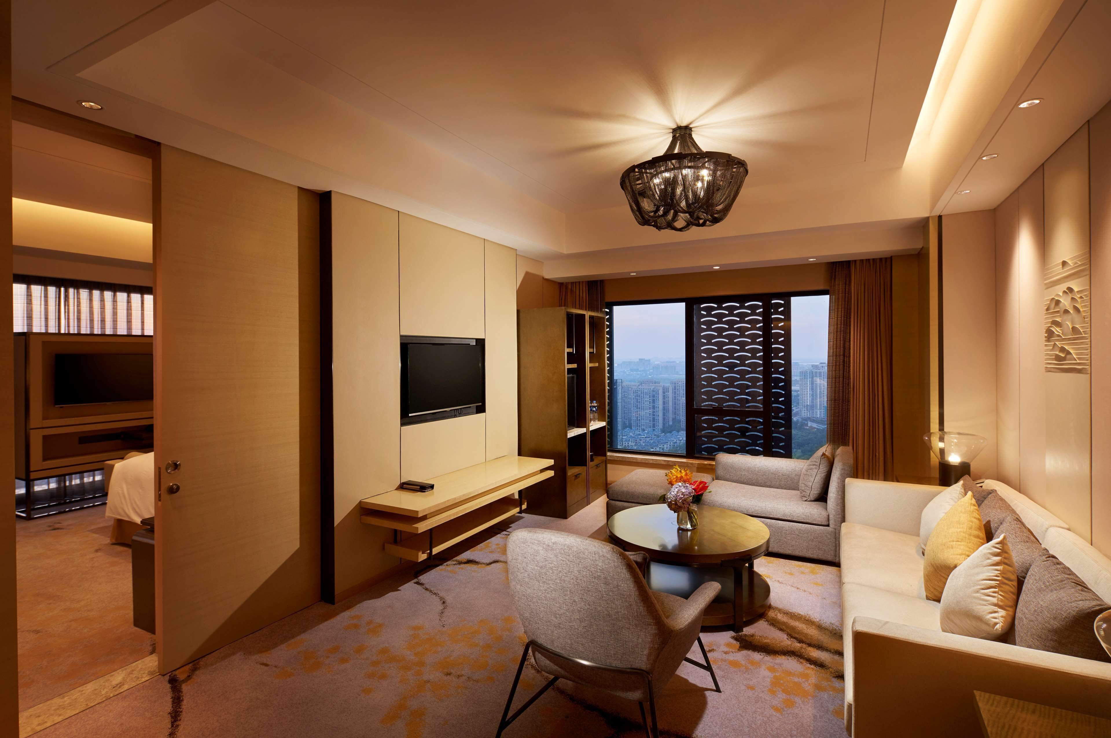 Een moderne hotelkamer met een flatscreen-tv, een bank, een eettafel en een groot raam met uitzicht op de stad.