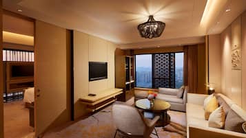 A modern hotel room with a flat-screen TV, a sofa, a dining table, and a large window offering a city view.