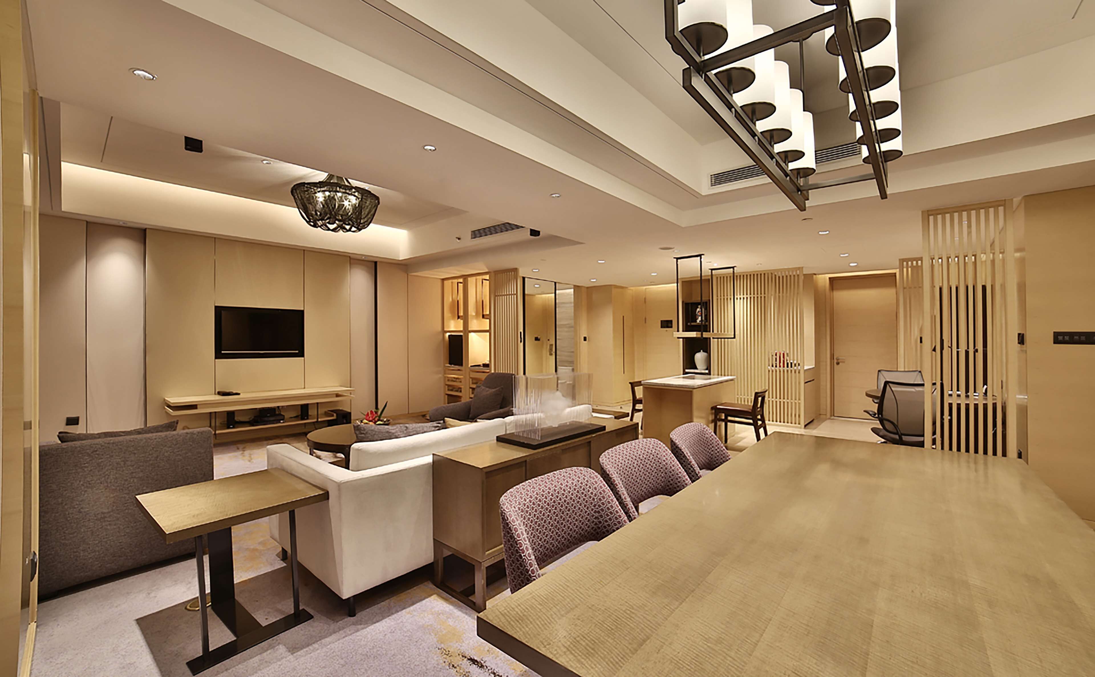 A modern living room with a large wooden dining table, sofas, a TV, and a chandelier.