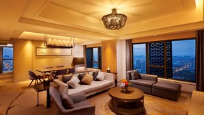 A modern hotel room with a large sofa, a dining table, and a view of the cityscape through large windows. - Hilton Suzhou (Suzhou)