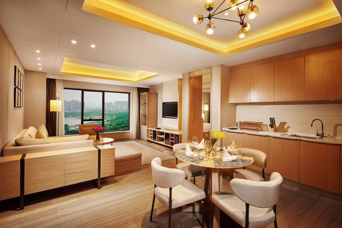 A modern living room with a sofa, dining table, and chairs. There is a TV and a window with a view of the city.
