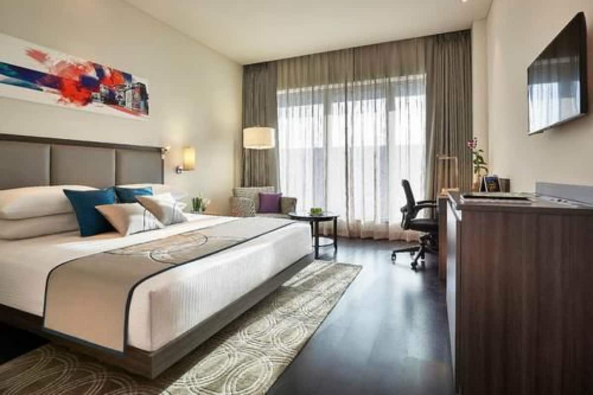 A hotel room with a large bed, a desk, a chair, and a television on the wall.