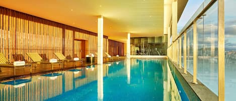 Une grande piscine intérieure dotée de chaises longues et d’un mur en bois.