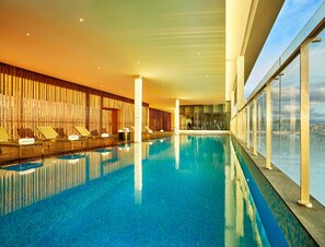 Una amplia piscina interior con sillones de descanso y una pared de madera.