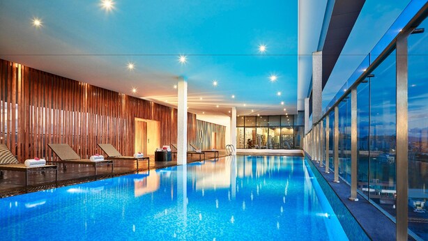An indoor swimming pool with lounge chairs and a view of the city.