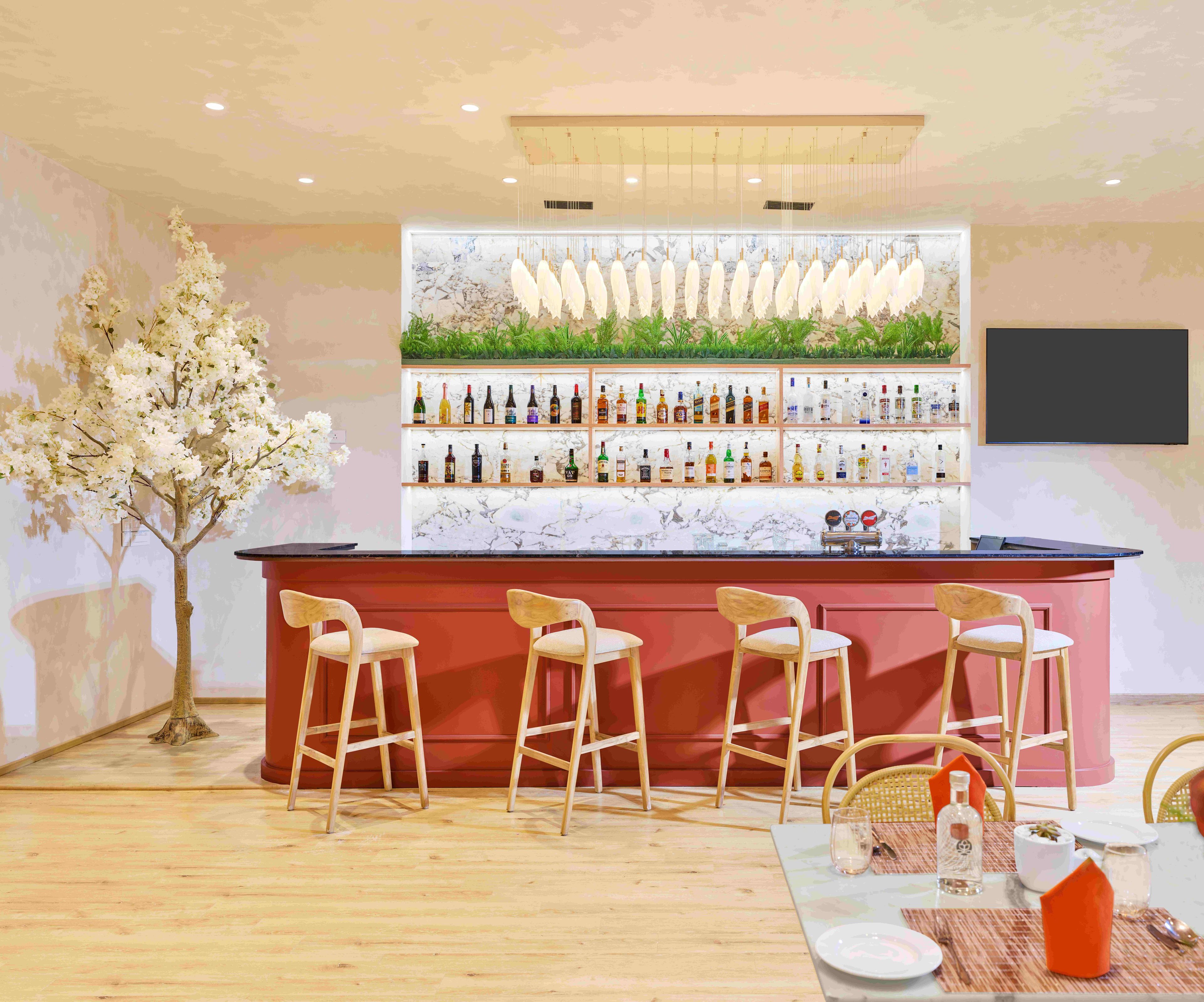Zona de bar con mostrador de mármol, varias estanterías llenas de botellas y taburetes de madera.