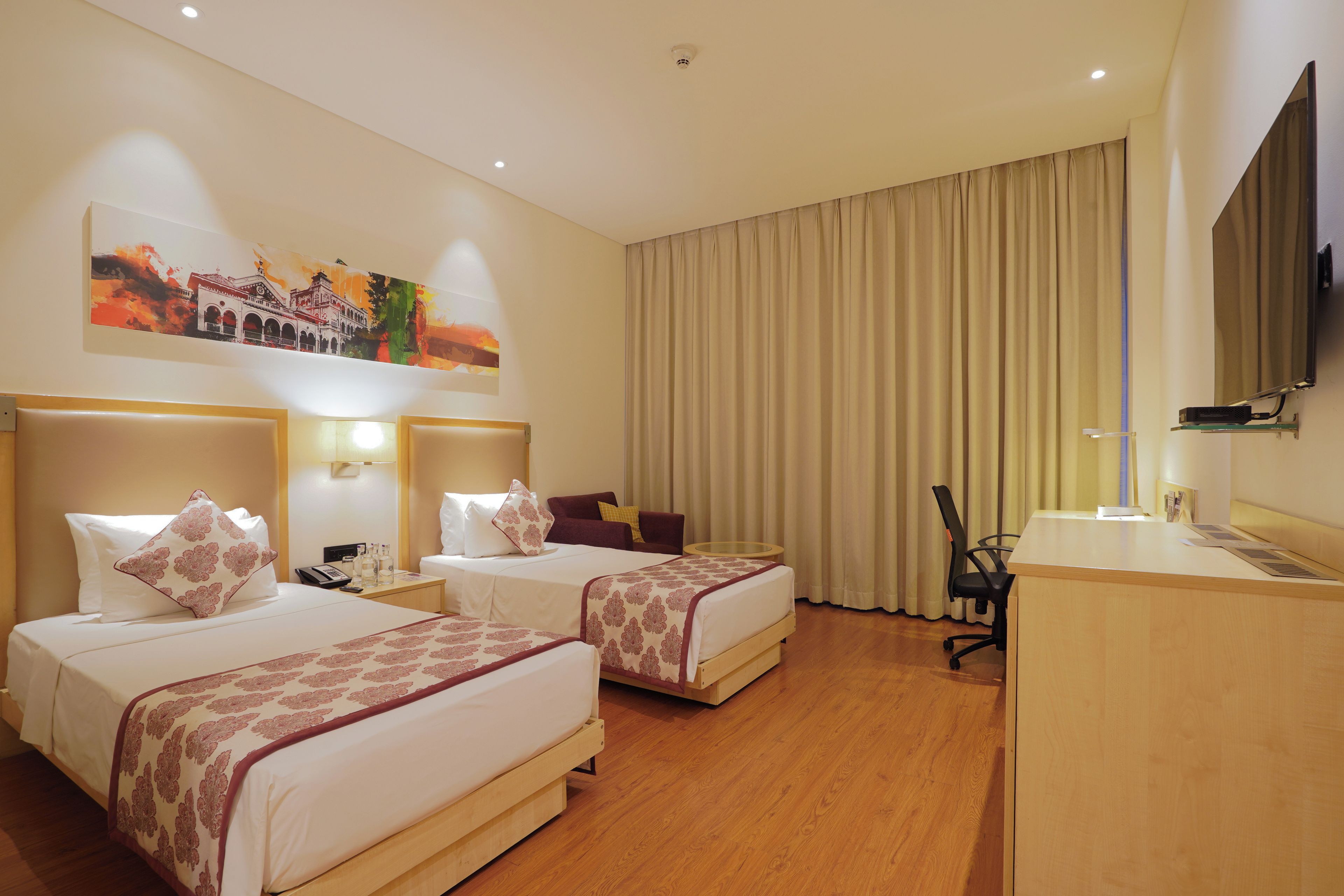 Habitación de hotel con dos camas, un escritorio, una silla, un televisor y un cuadro en la pared.