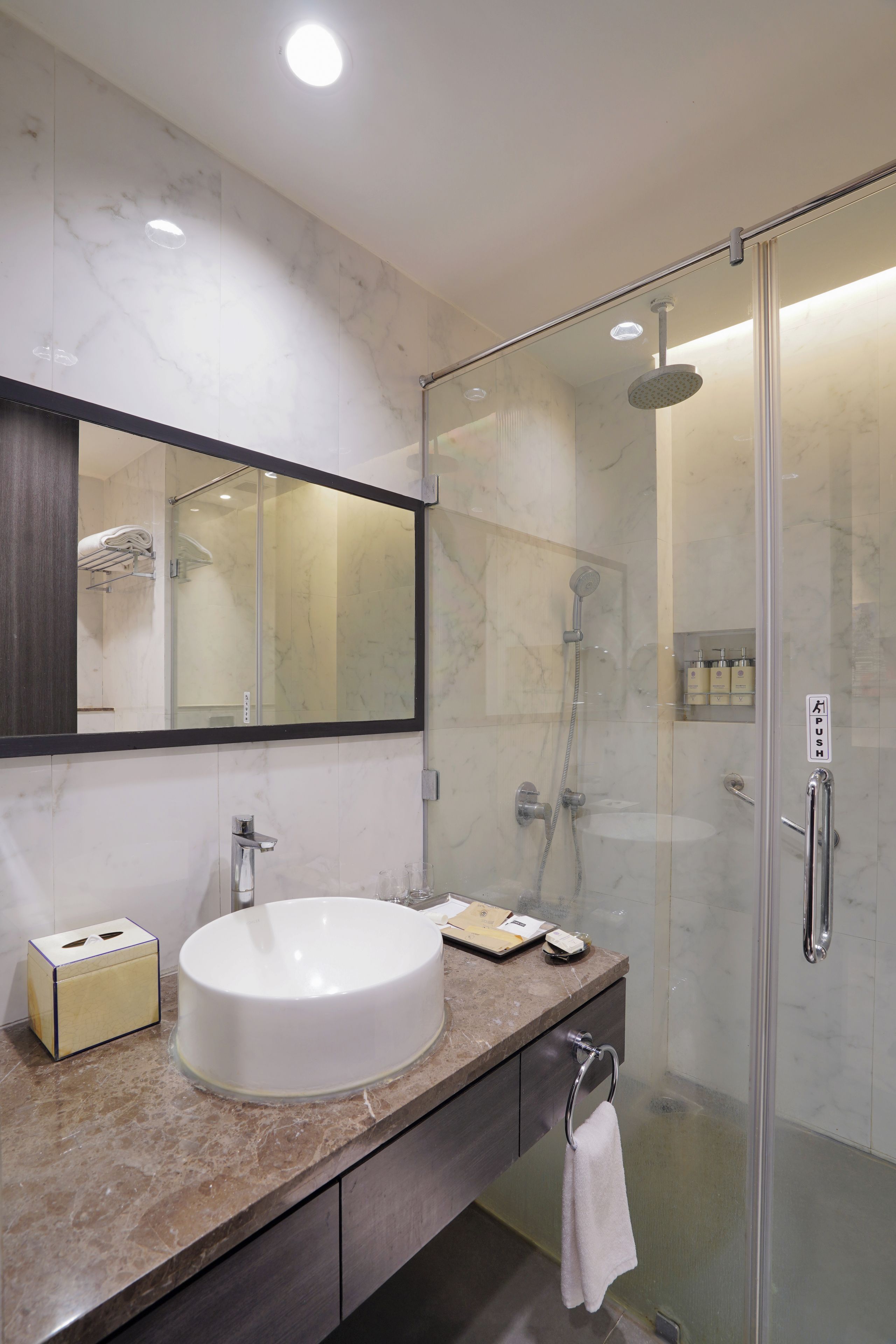 A modern bathroom with a large mirror, a sink, a glass-enclosed shower, and a towel rack.