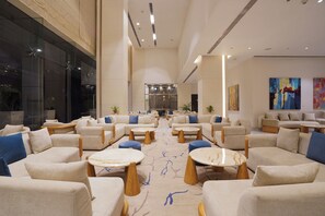 A spacious lobby with multiple seating areas, a central reception desk, and a large window providing a view of the outside. - Vivanta Pune, Hinjawadi (Paud)