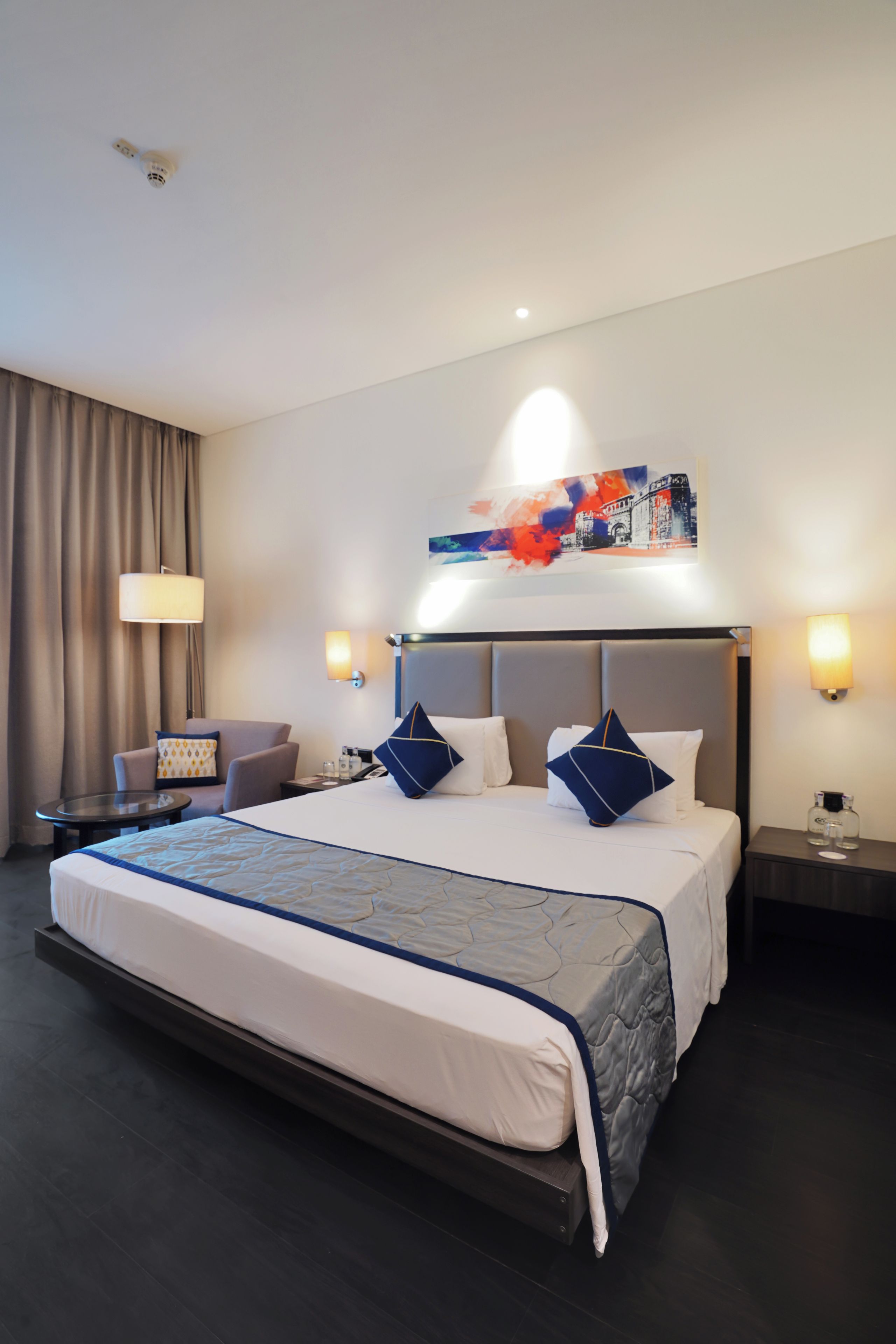 Une chambre d’hôtel avec un grand lit, un bureau, une chaise, une lampe et un tableau au mur.