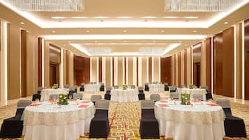 A conference room with multiple tables, black chairs, and chandeliers.