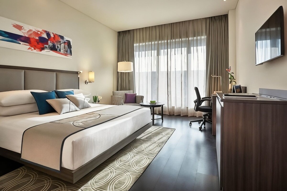 A hotel room with a large bed, a desk, a chair, and a TV.