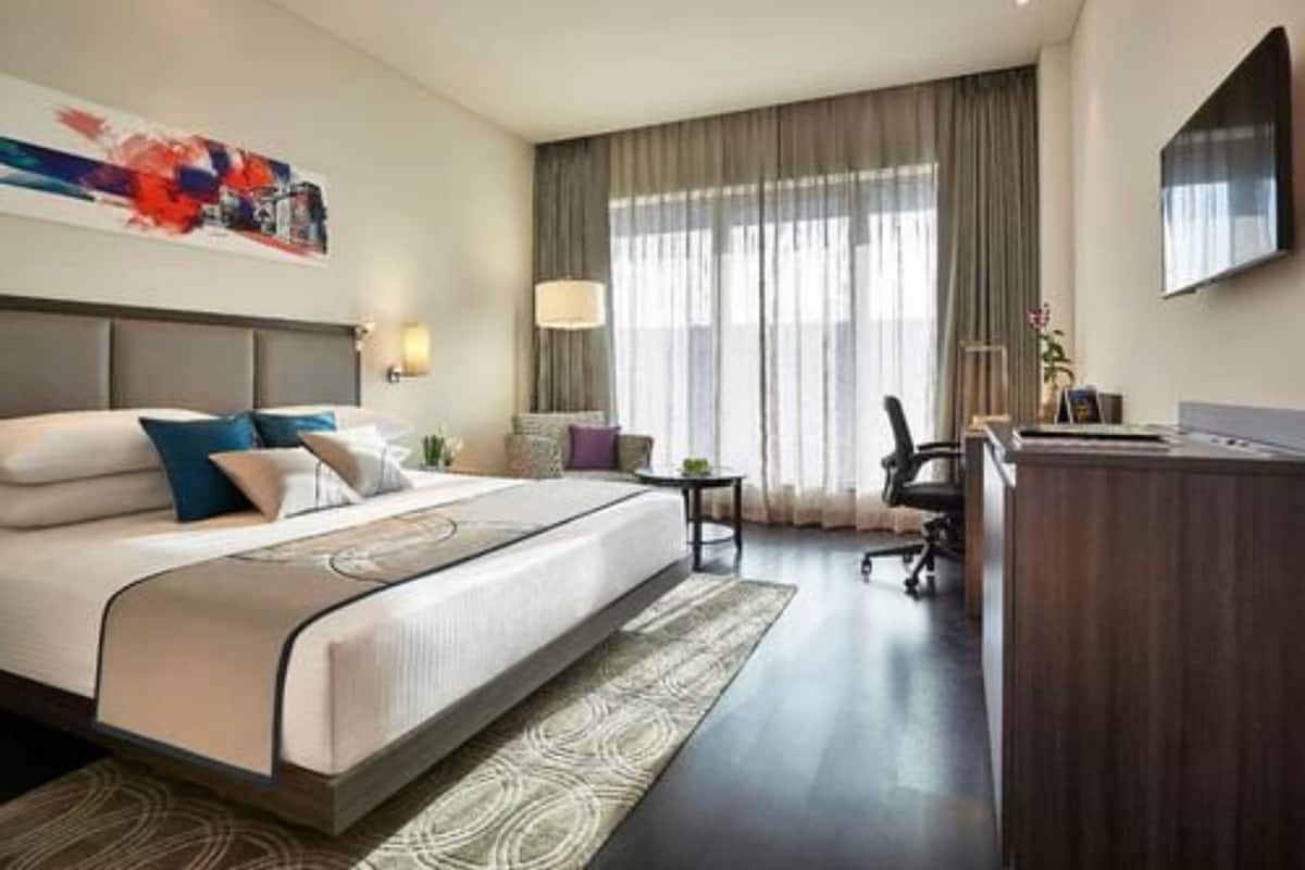 A hotel room with a bed, a desk, a chair, a TV, and a window with curtains.