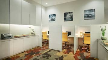 A modern office space with white cabinets, desks, and chairs. There are three framed pictures on the wall, a printer on the counter, and a patterned carpet.
