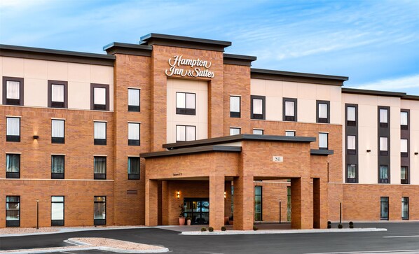 A Hampton Inn & Suites building with a brick facade, multiple windows, and a clear sky.