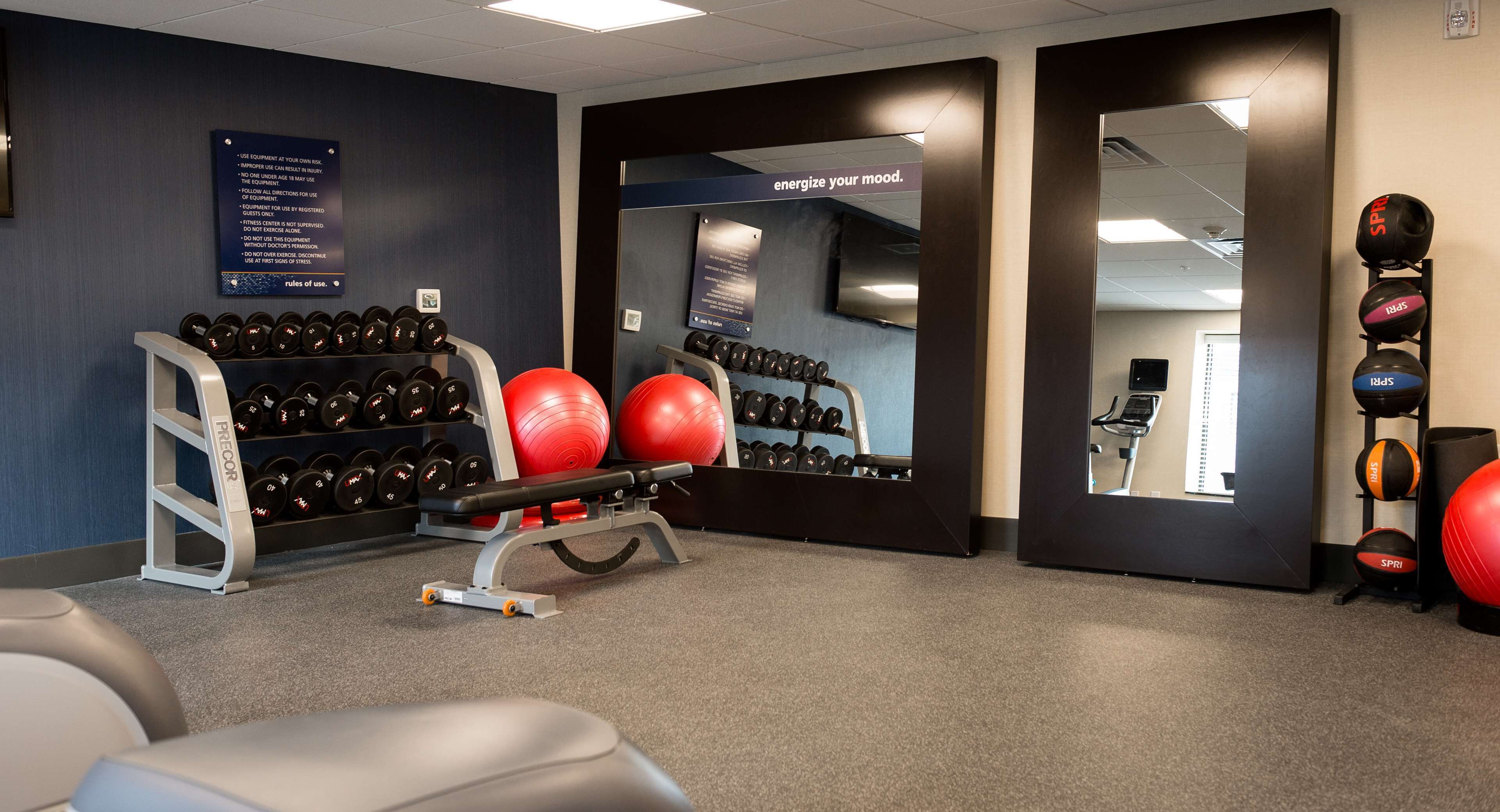 Un gimnasio con equipo de ejercicio, un espejo y una pared con un letrero motivacional.
