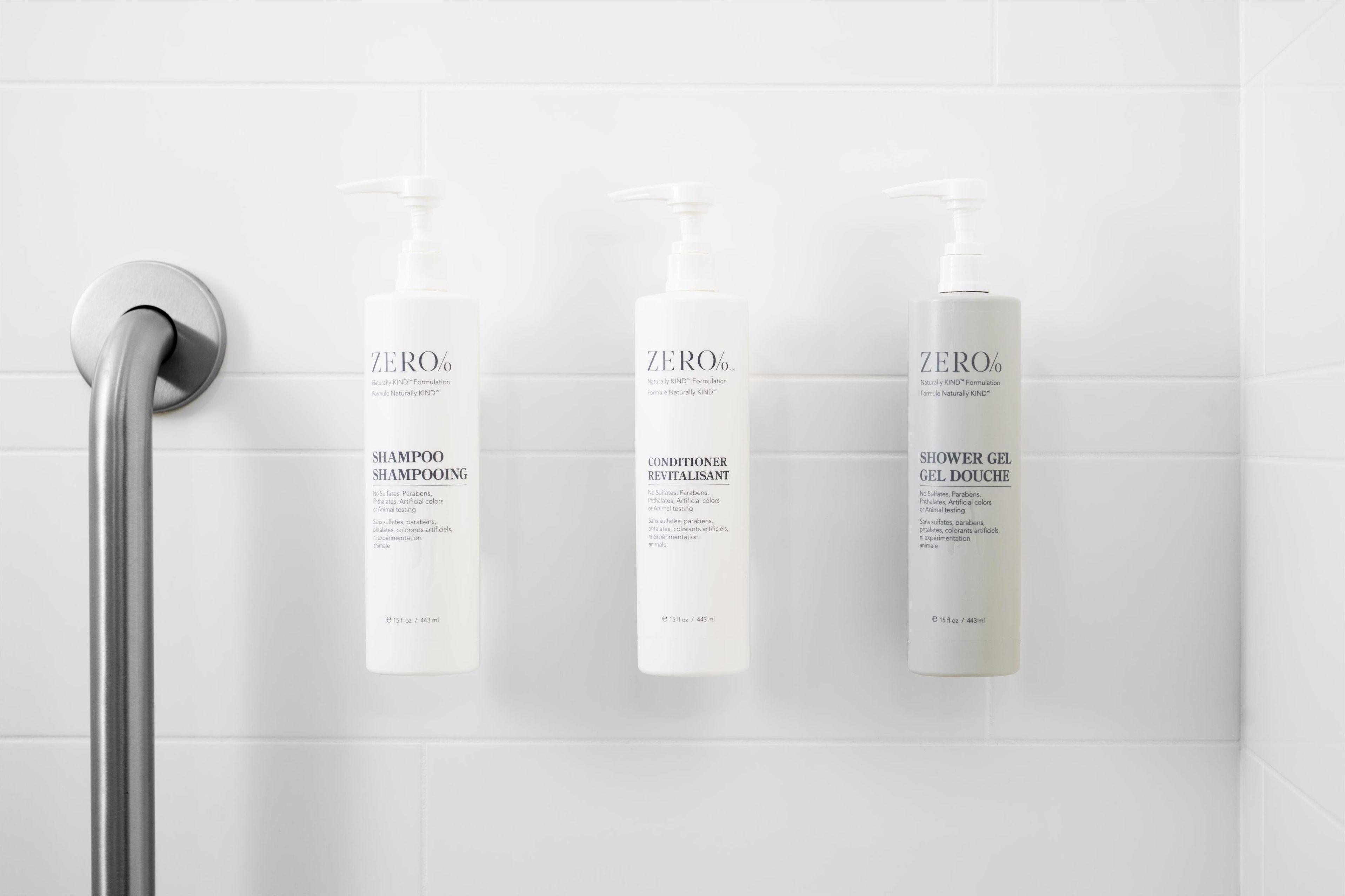 Three bottles of ZERO% products: shampoo, conditioner, and shower gel, mounted on a white tiled wall.