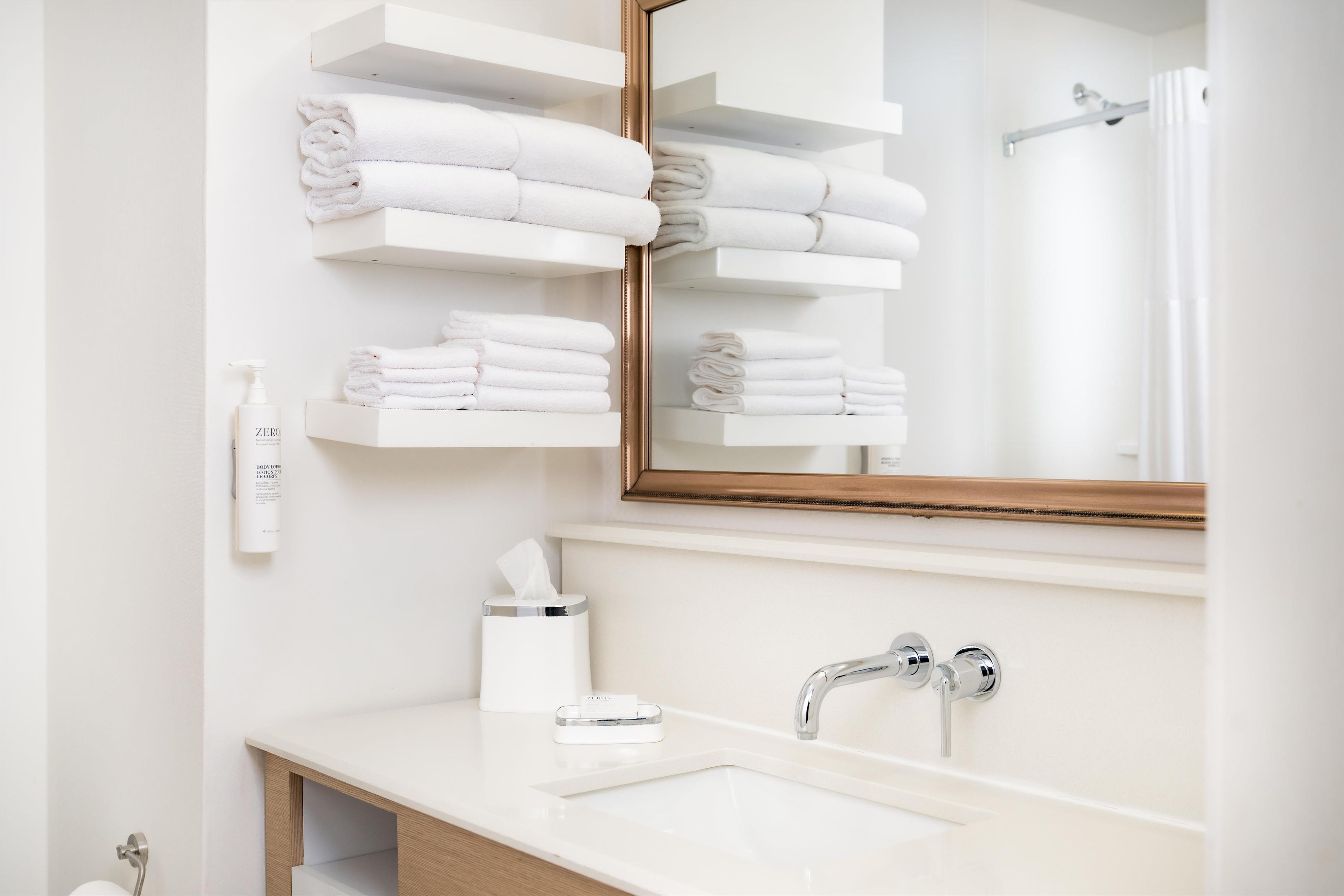 A modern bathroom with a white sink, a mirror, and shelves holding neatly folded towels.