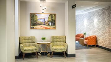 A lobby with two armchairs, a small table, and a painting of a street scene.