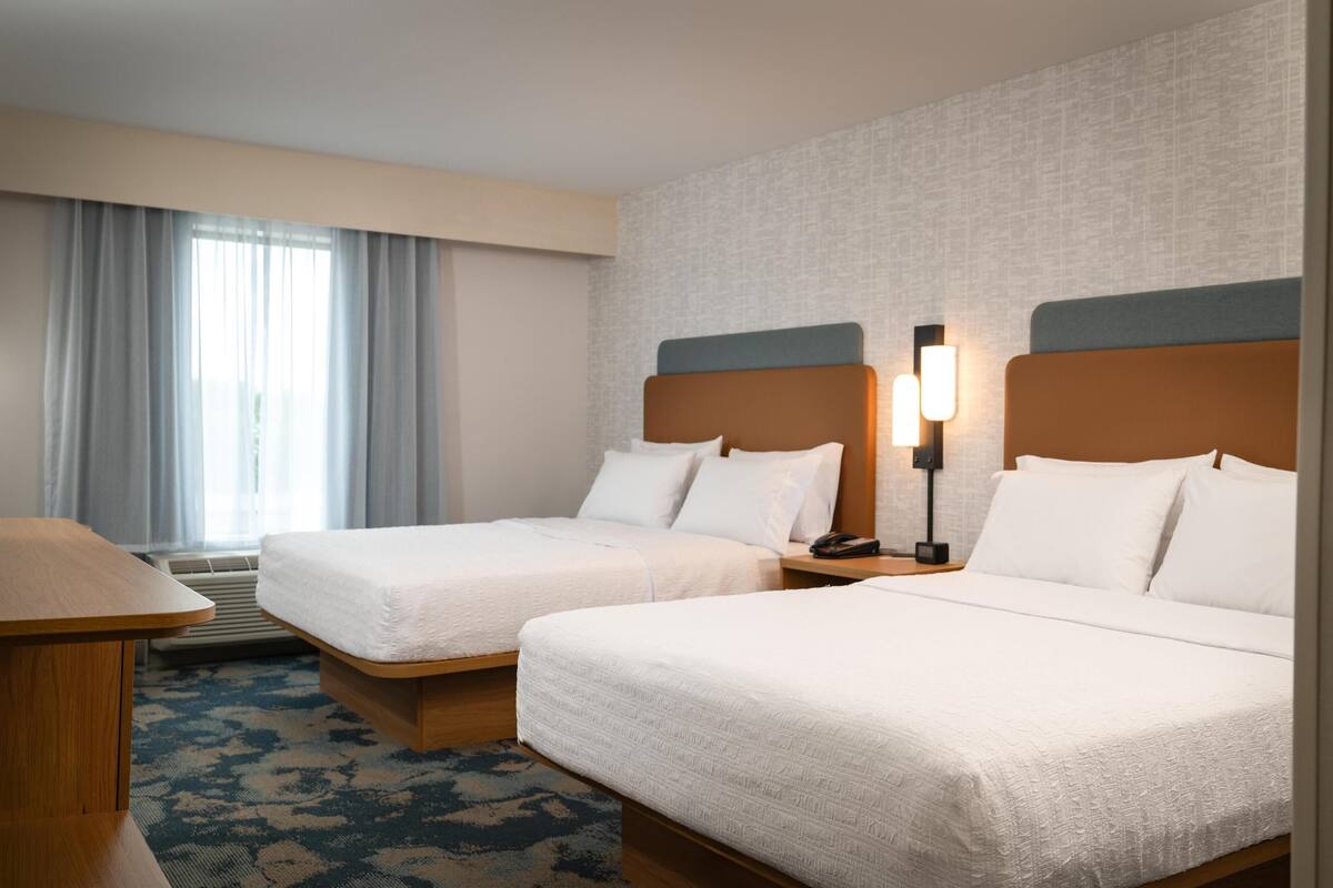 A hotel room with two beds, a desk, and a window with curtains.