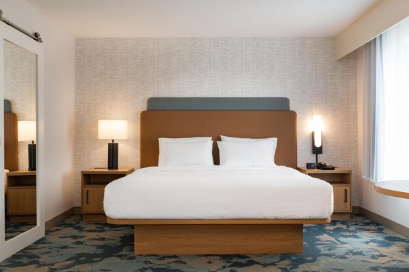 A hotel room with a large bed, two bedside tables with lamps, a mirror, and a window with curtains.