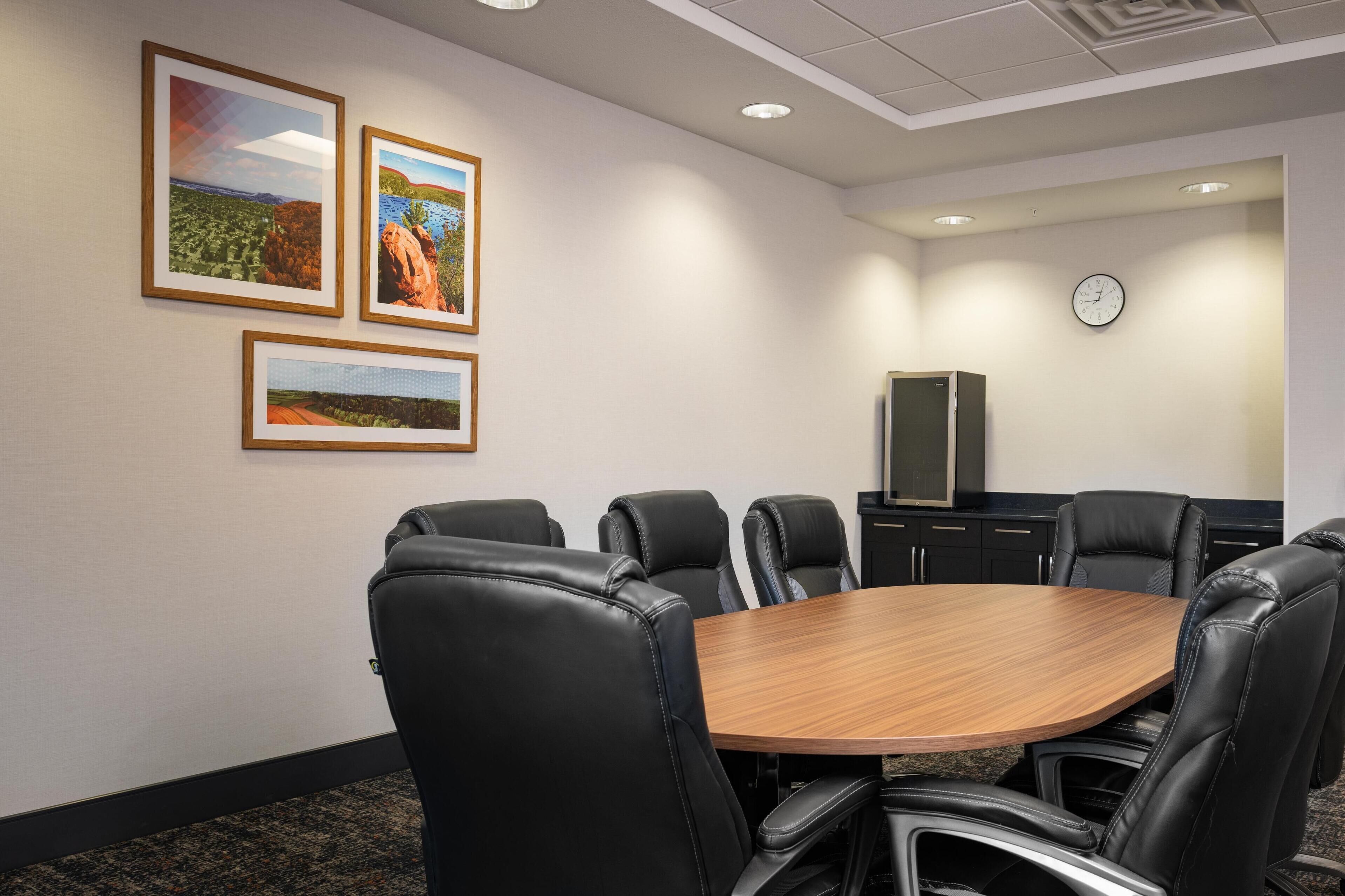 Une salle de conférence avec une table en bois et des fauteuils en cuir noir, des tableaux encadrés au mur, une horloge et un meuble.