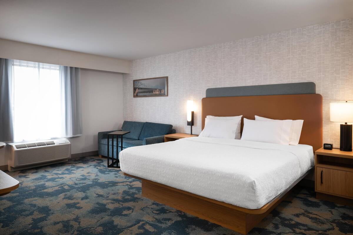 A hotel room with a large bed, a desk, a chair, a small table, and a window with curtains.