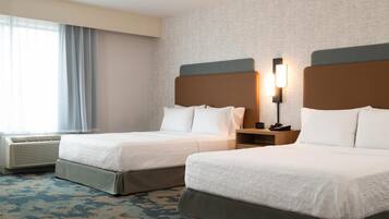 A hotel room with two beds, a nightstand, a lamp, and a window with curtains.