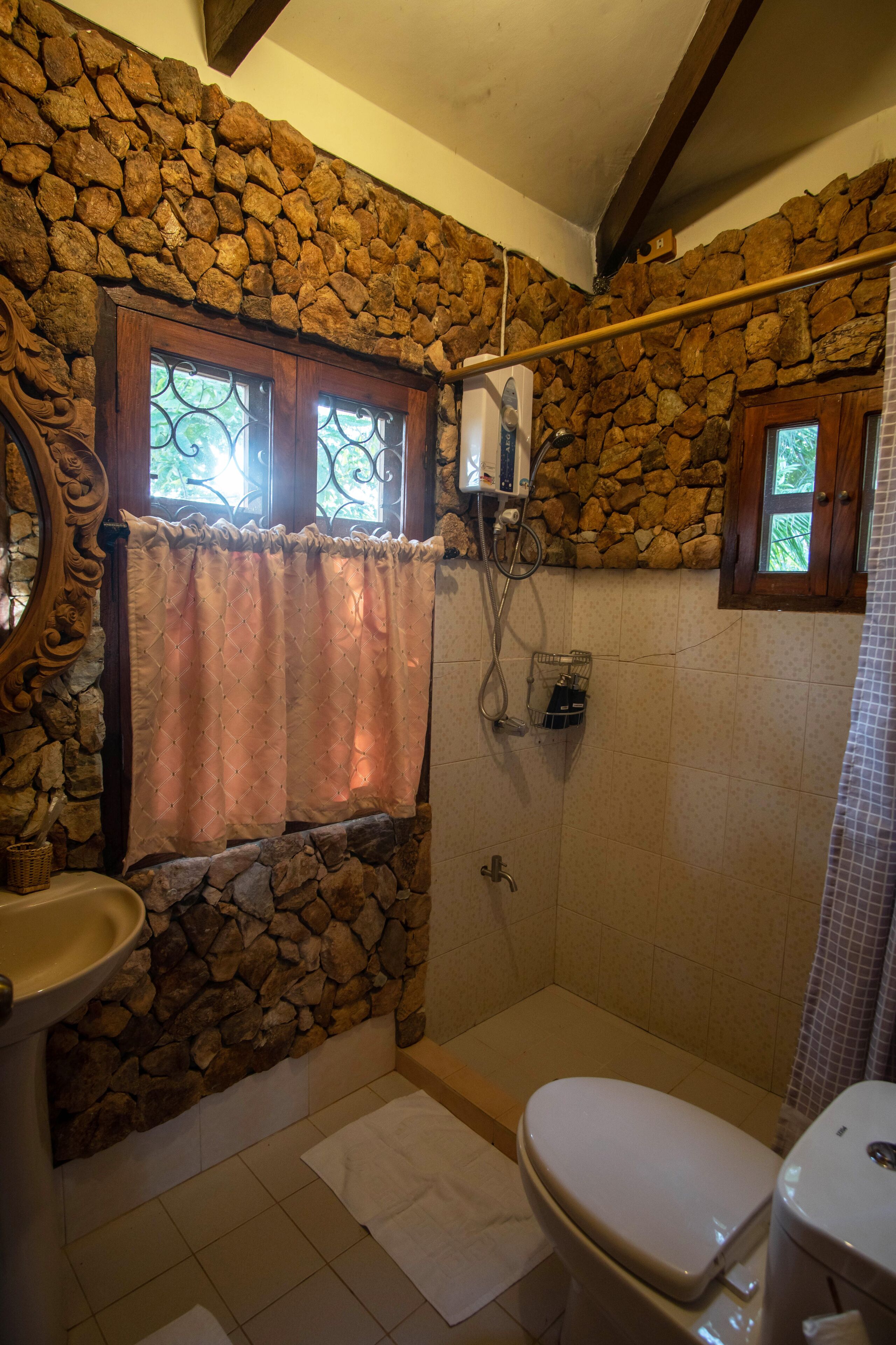 Une salle de bain avec un mur en pierre, une fenêtre avec un rideau, un lavabo et des toilettes.