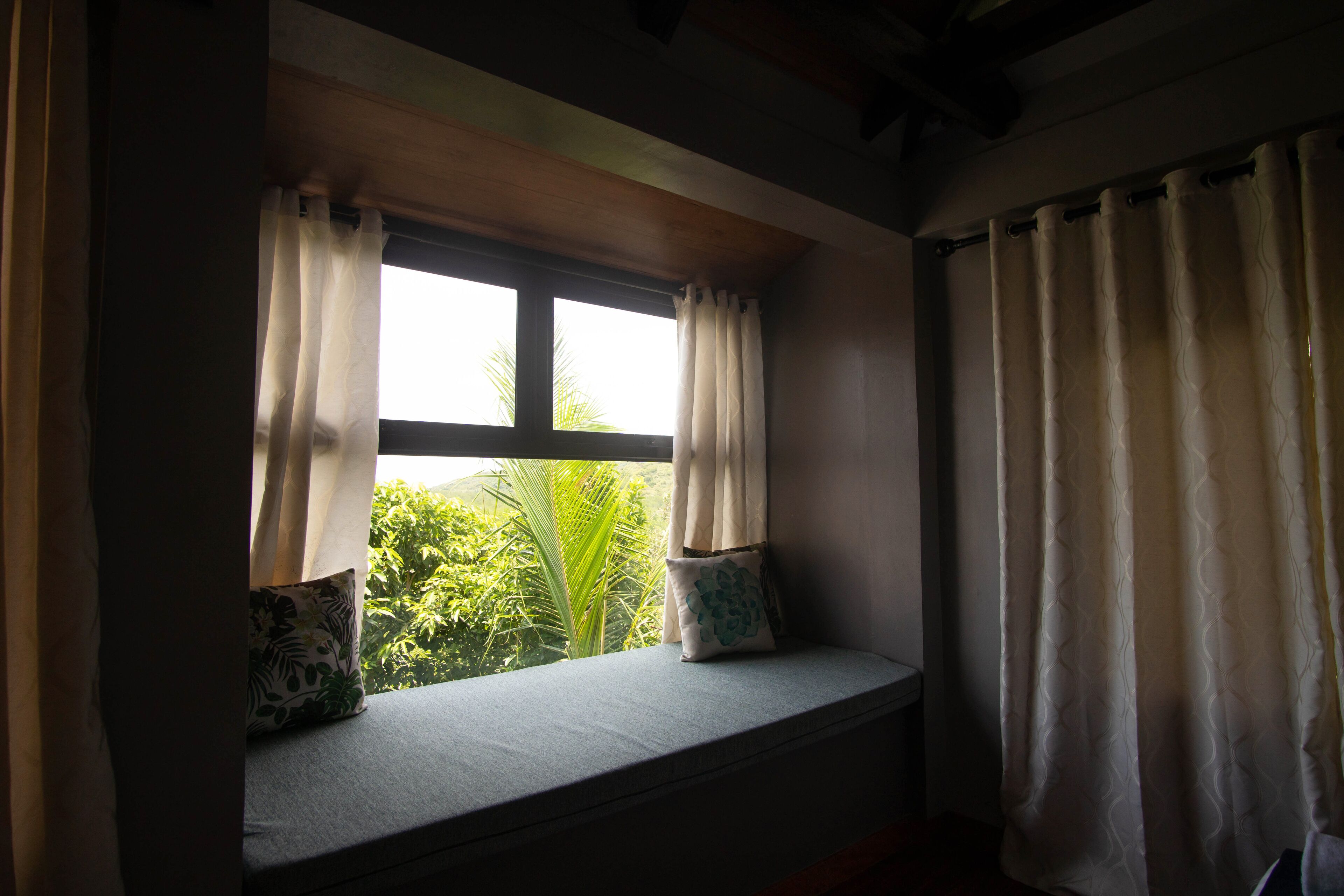 A room with a window seat, two pillows, and a view of greenery outside.