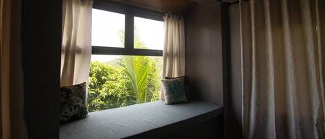 A room with a window seat, two pillows, and a view of greenery outside.