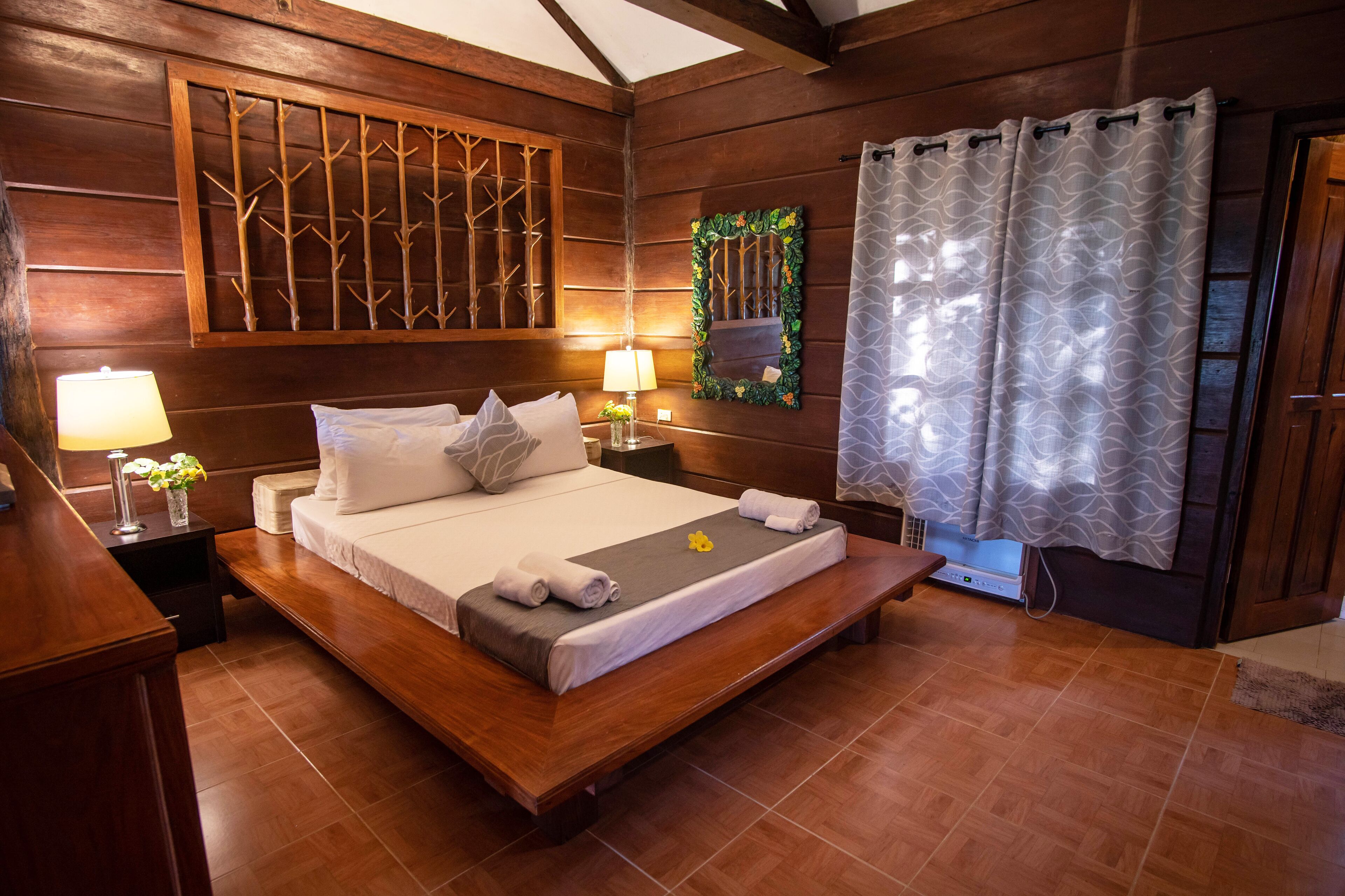A wooden-paneled bedroom with a large bed, bedside lamps, a mirror, and a window with curtains.