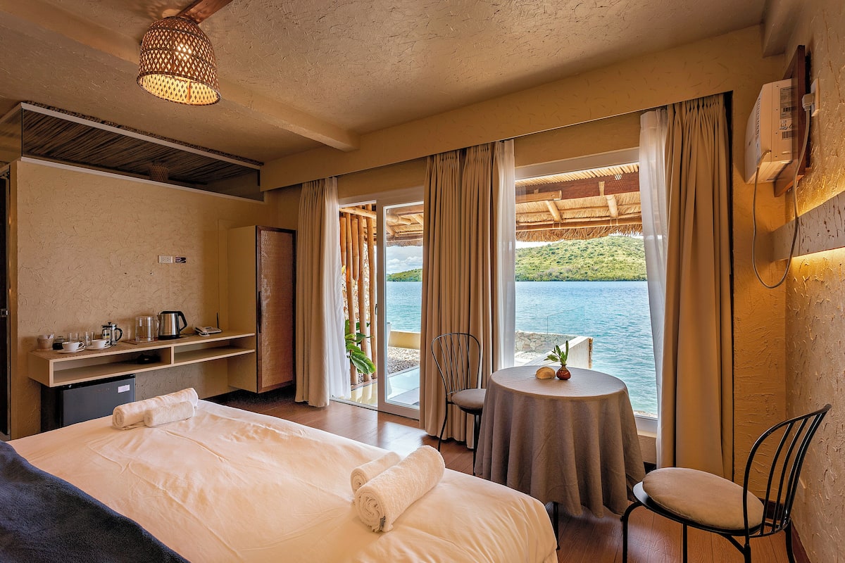Een hotelkamer met een bed, een bureau, een stoel, een tafeltje en uitzicht op zee.