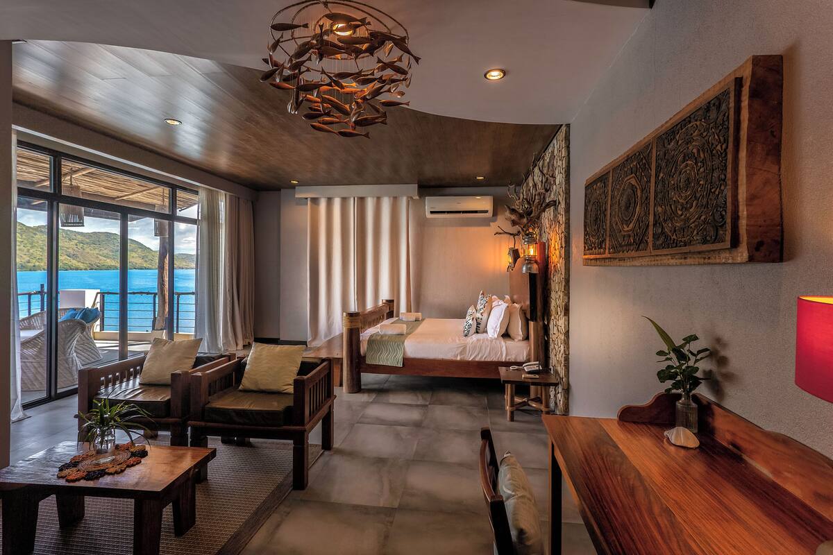 Een ruime slaapkamer met een groot bed, een zithoek met uitzicht op zee en een houten plafond.