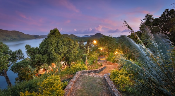 A scenic view of a lakeside area with stone pathways, lush greenery, and distant mountains.