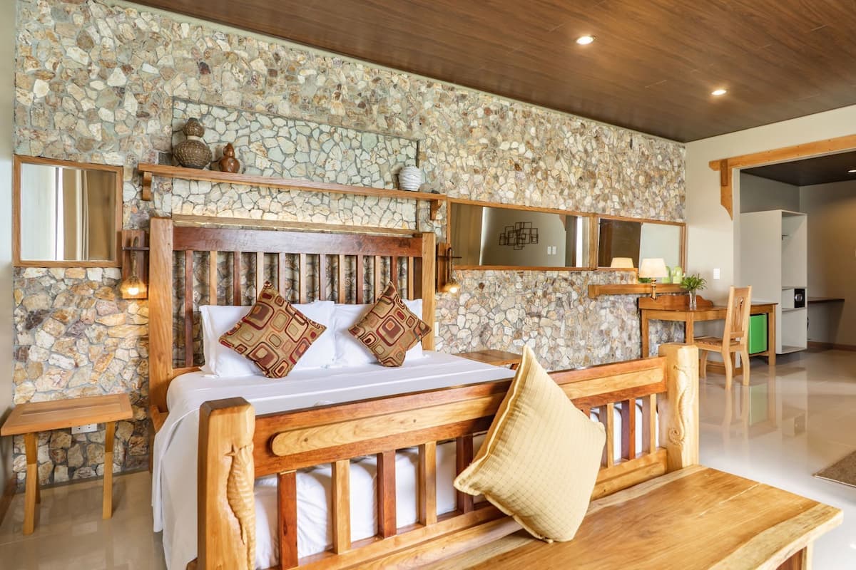 Een slaapkamer met een stenen muur, een houten hoofdbord en een houten bankje.