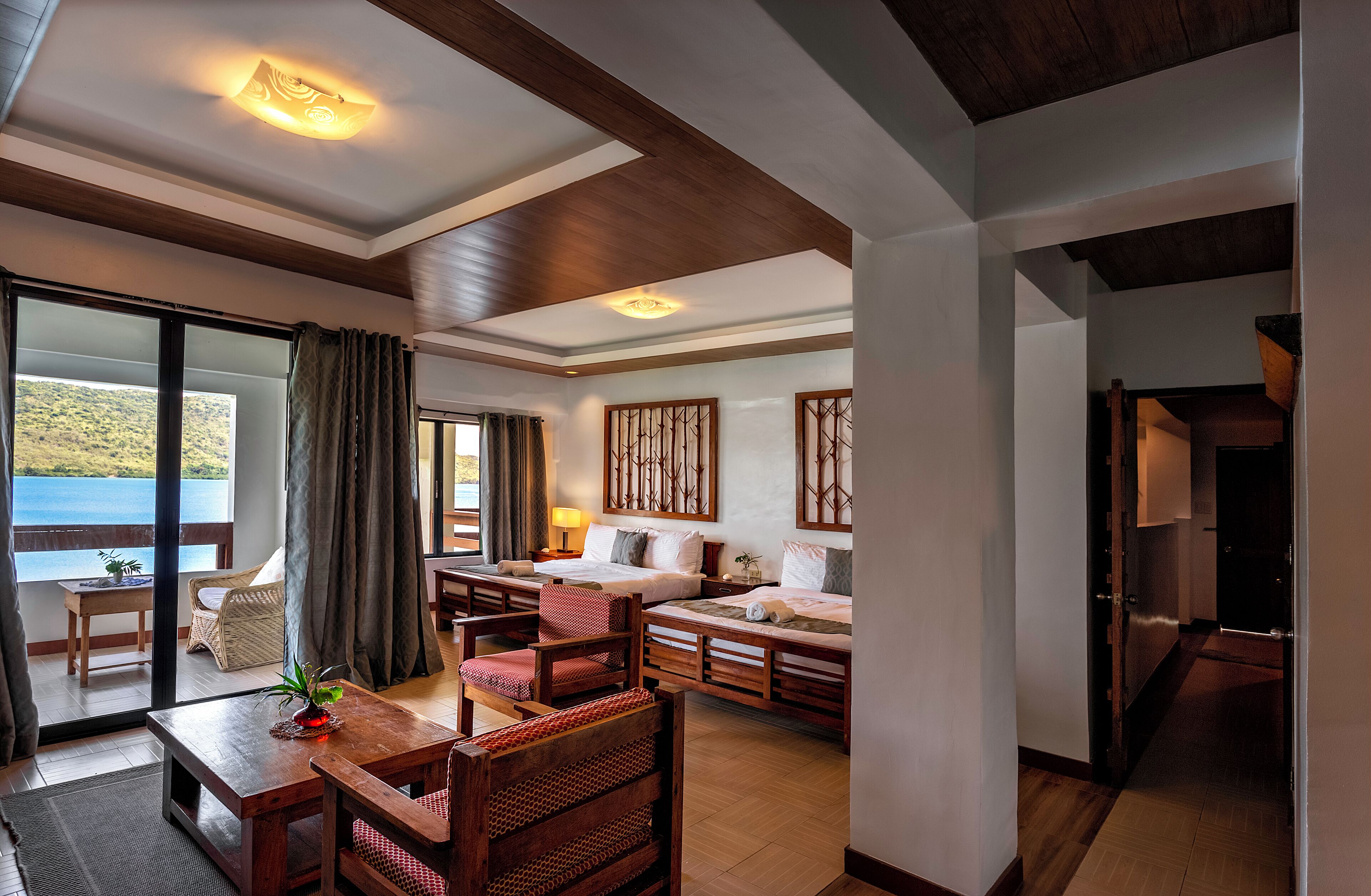 A hotel room with a balcony, wooden furniture, and a view of the sea.