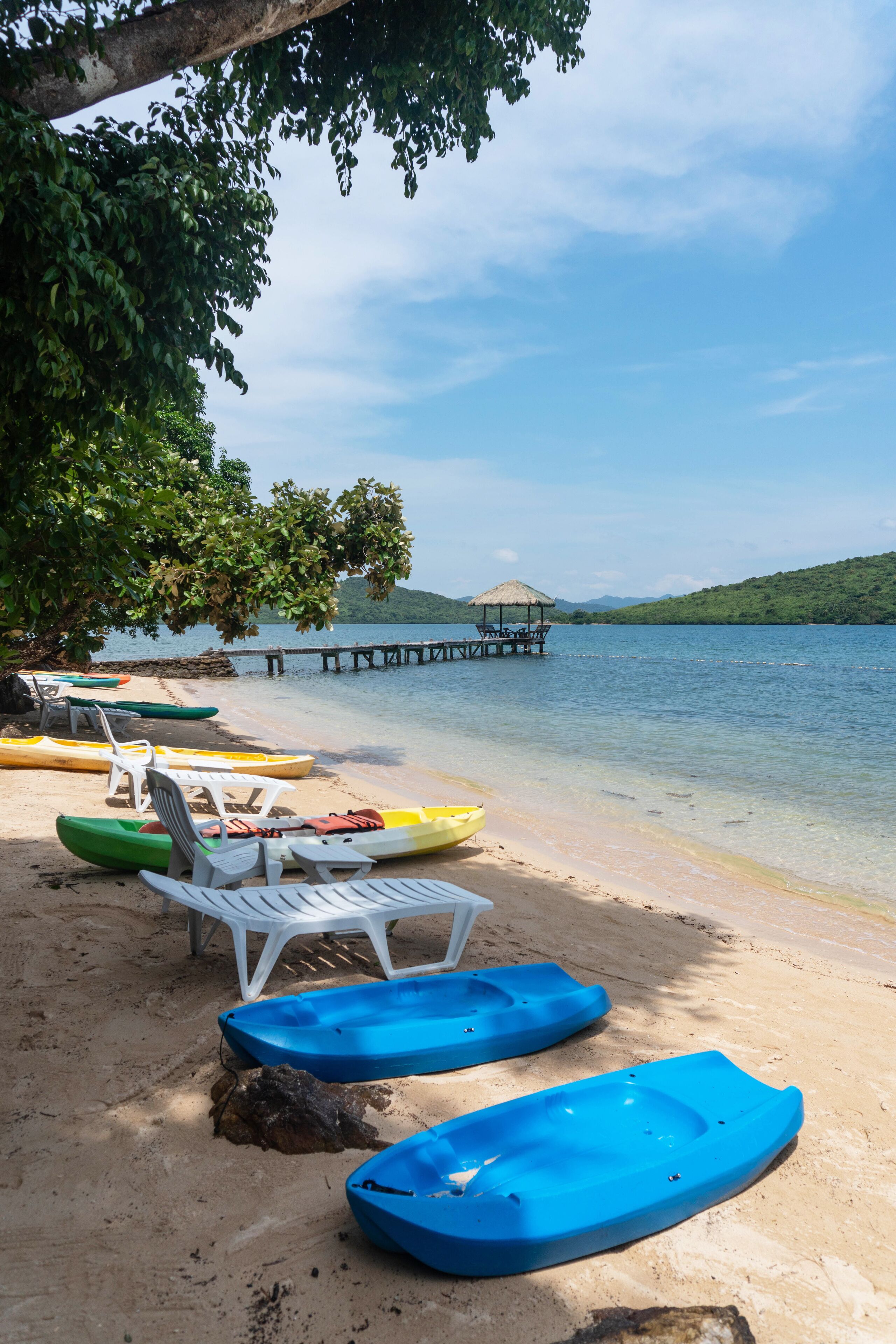 A beach with kayaks, lounge chairs, and a pier extending into the water.