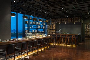A bar area with a long counter, stools, and shelves with kitchenware. - Renaissance Suzhou Wujiang Hotel (Suzhou)