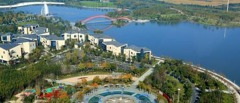 Vista aérea de una zona junto al lago con edificios residenciales, un parque con áreas de juegos y un puente al fondo.