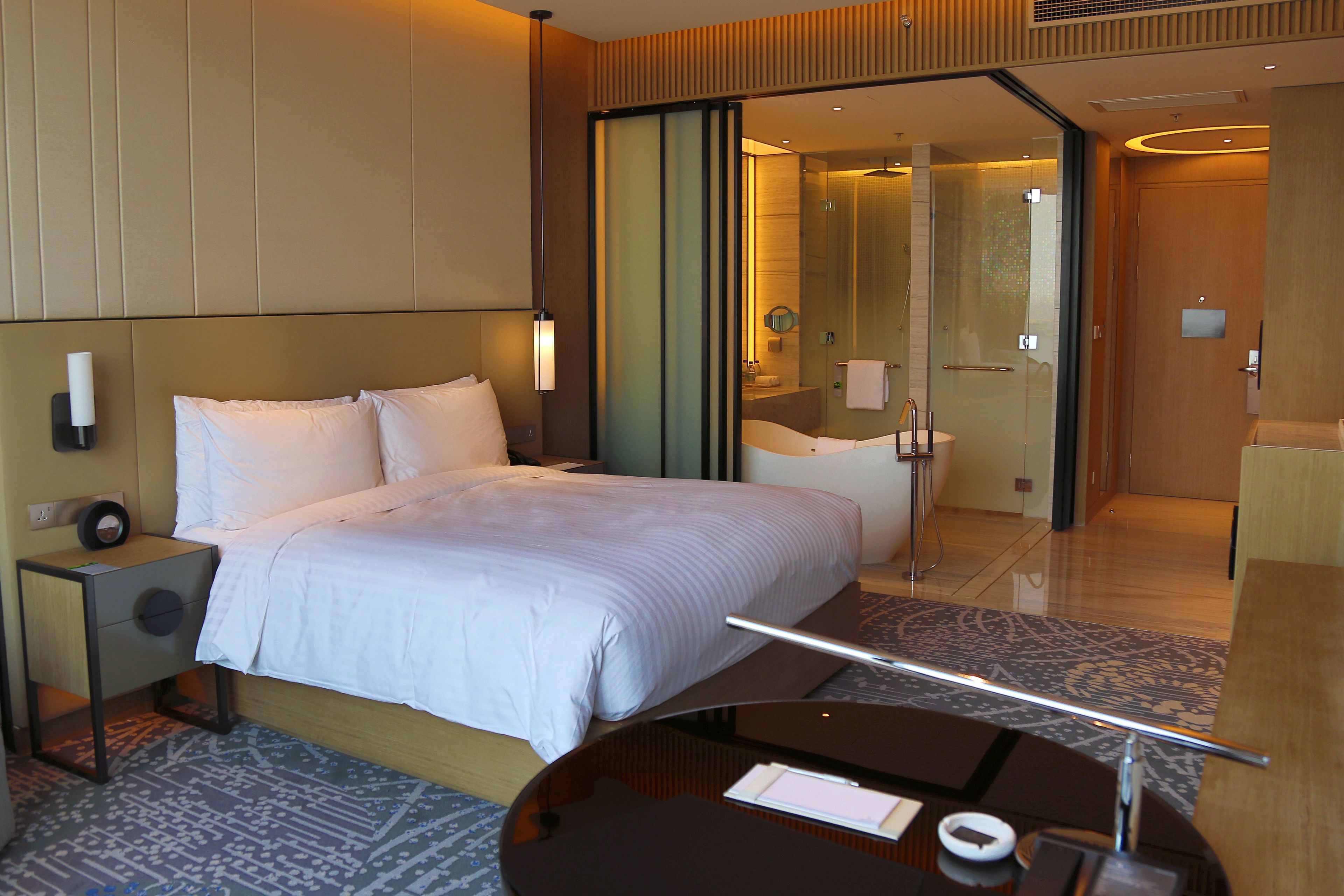 A hotel room with a bed, bedside table, and a desk with a chair.