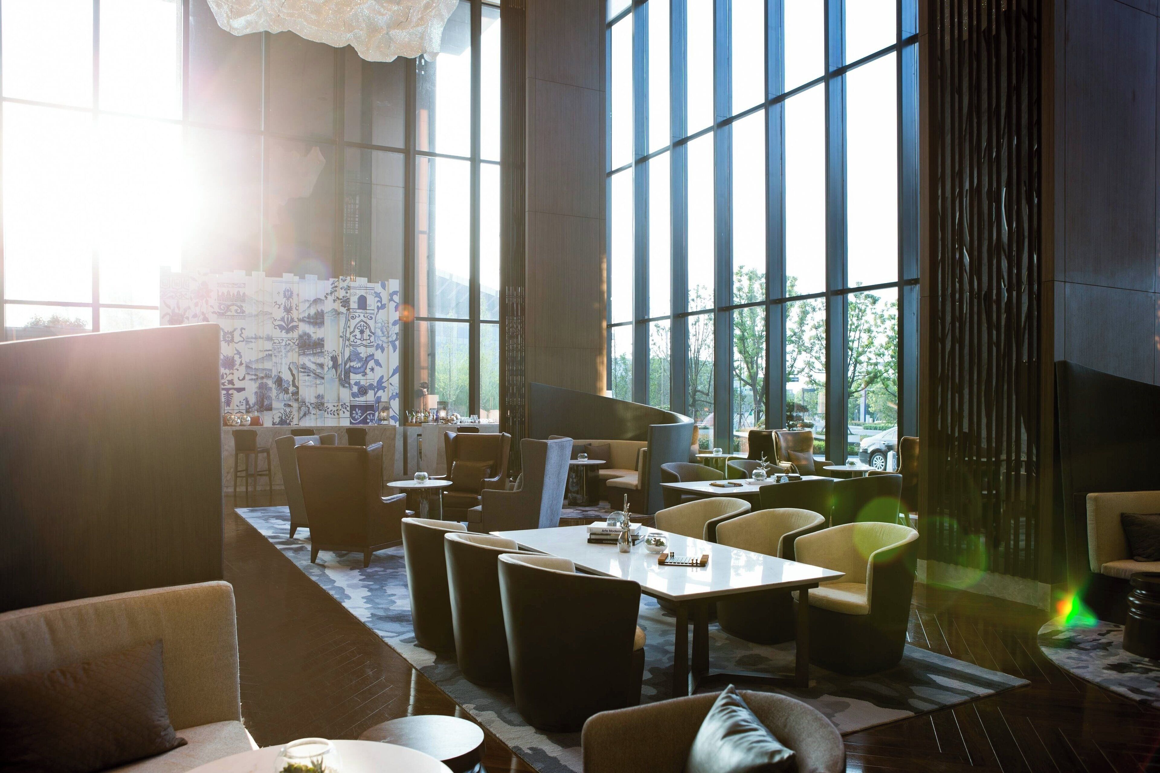 A modern interior with large windows, a mix of seating arrangements, and a patterned wall.