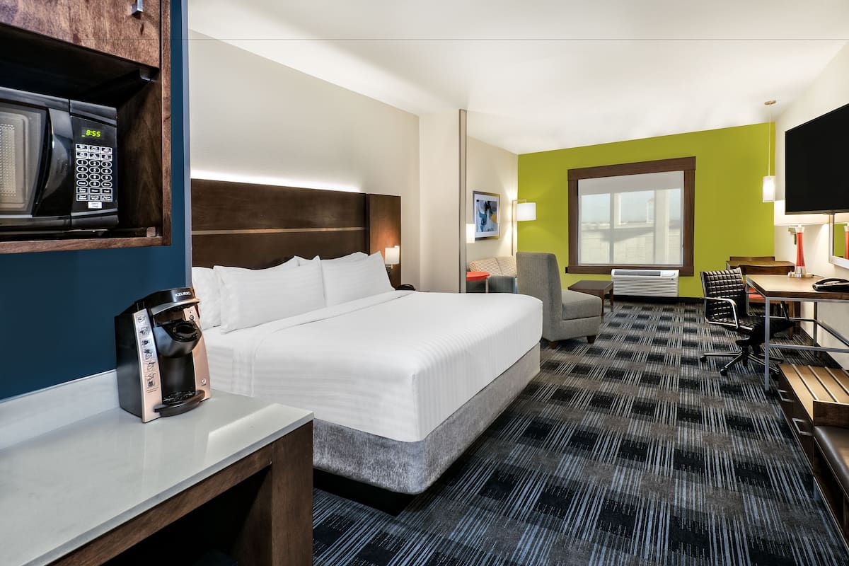 A hotel room with a large bed, a desk with a chair, a coffee maker, a TV, and a window.
