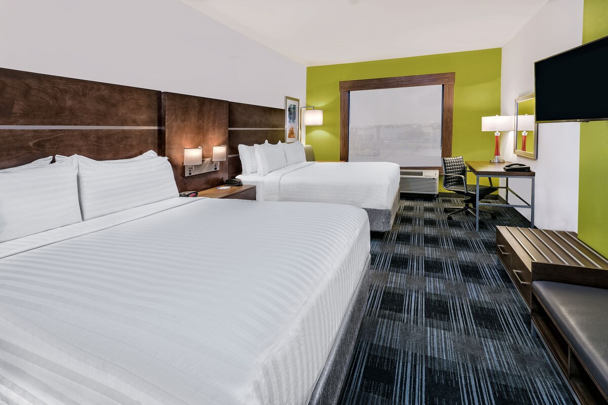 A hotel room with two beds, a desk, a chair, a TV, and a large window.