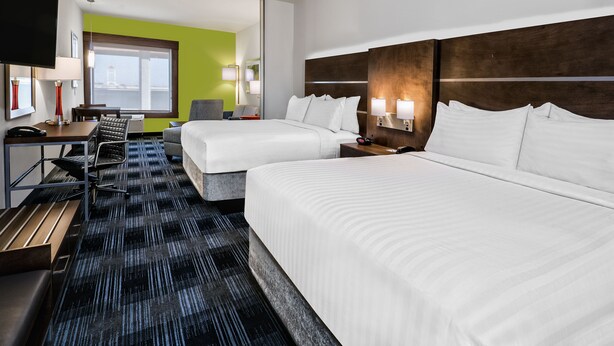 A hotel room with two beds, a desk with a chair, a TV, and a large window with a view.