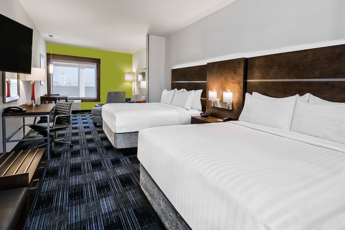 A hotel room with two beds, a desk with a chair, a TV, and a large window with a view.