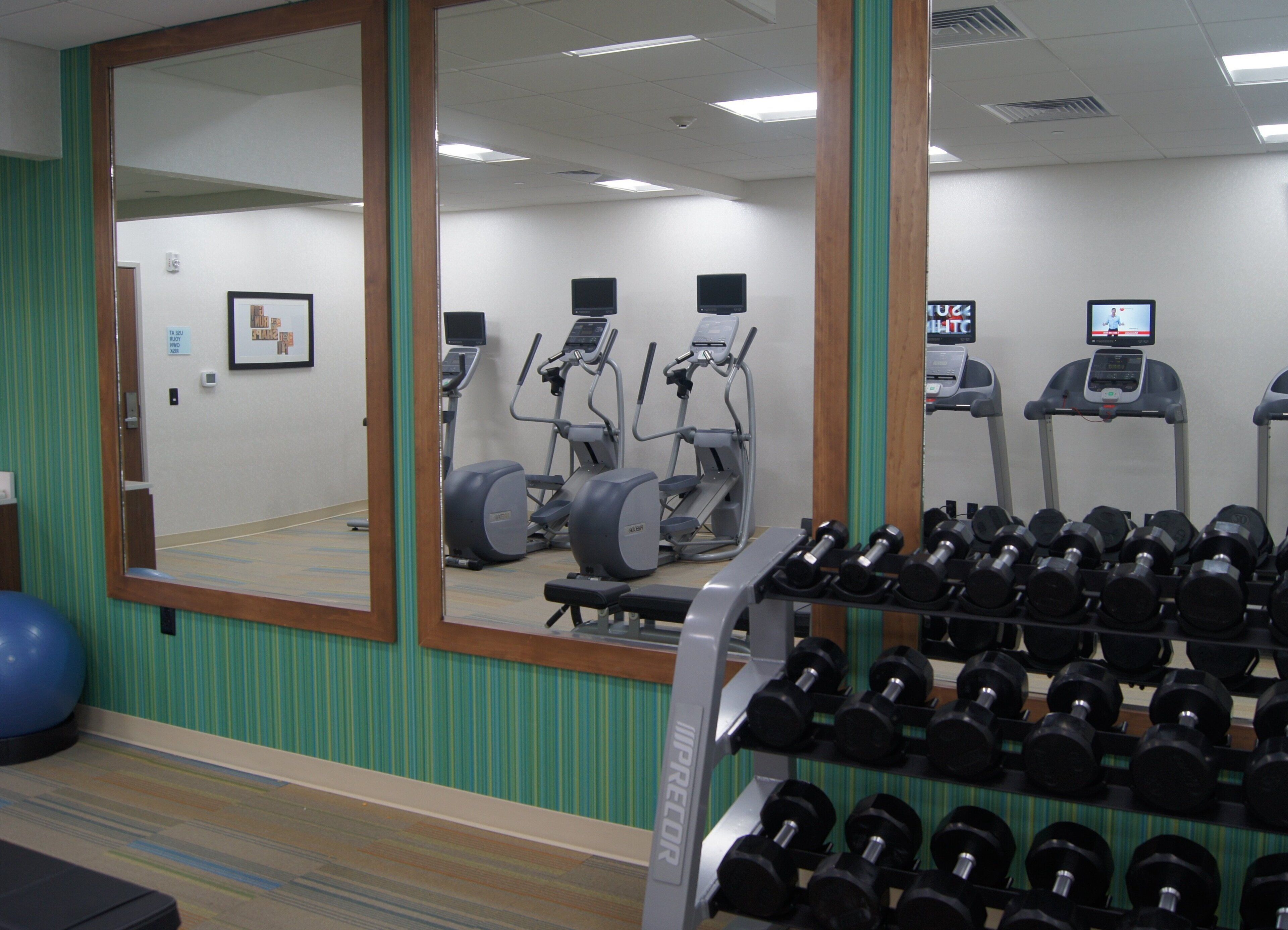 Un gimnasio con equipo de ejercicio, un espejo y un estante con mancuernas.