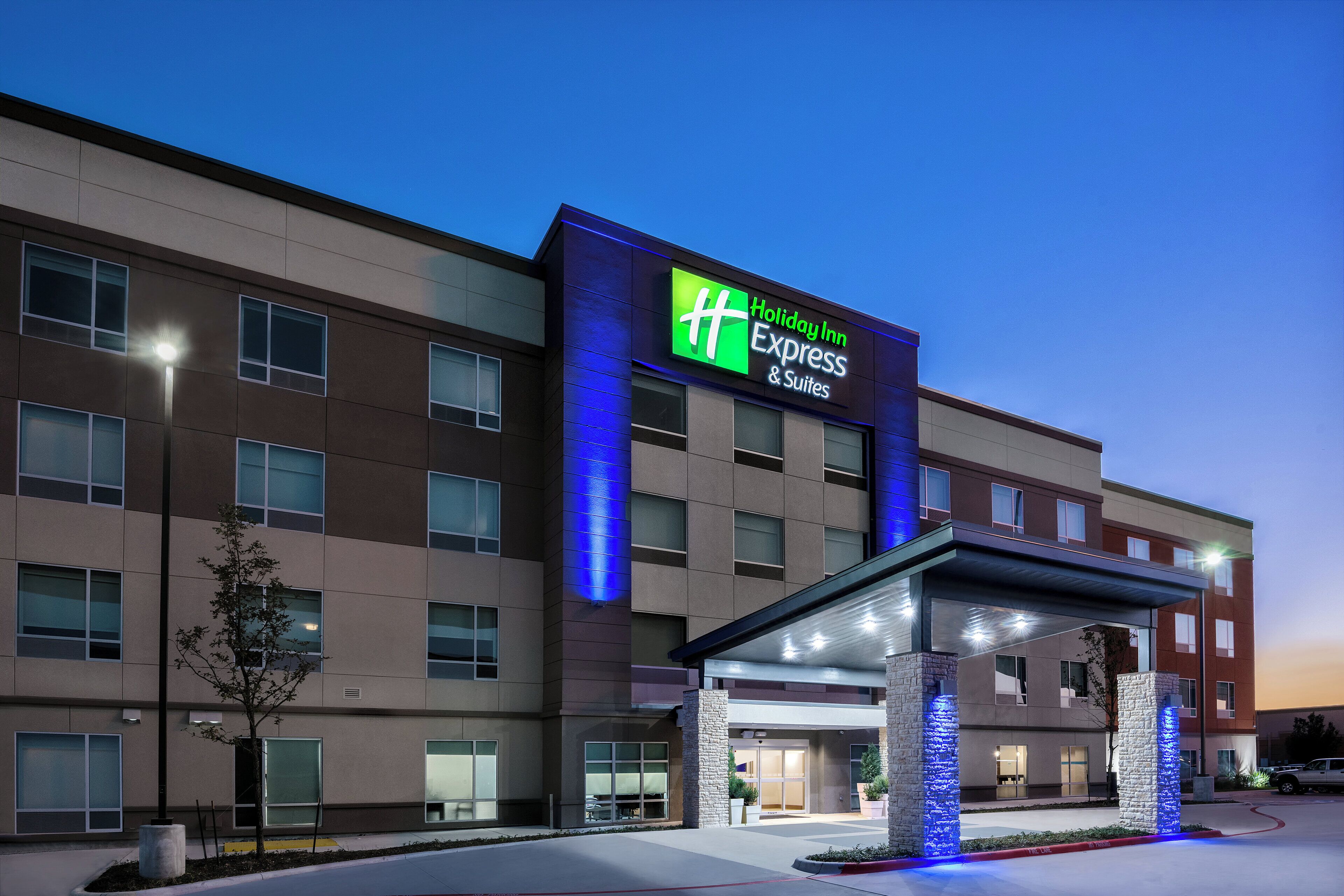 A Holiday Inn Express & Suites hotel with a modern facade, large windows, and a covered entrance area.