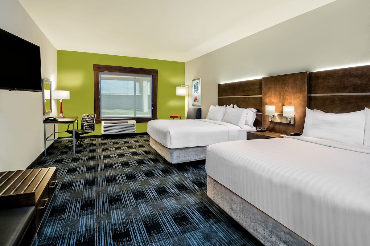A hotel room with two beds, a desk, a chair, a TV, and a window.