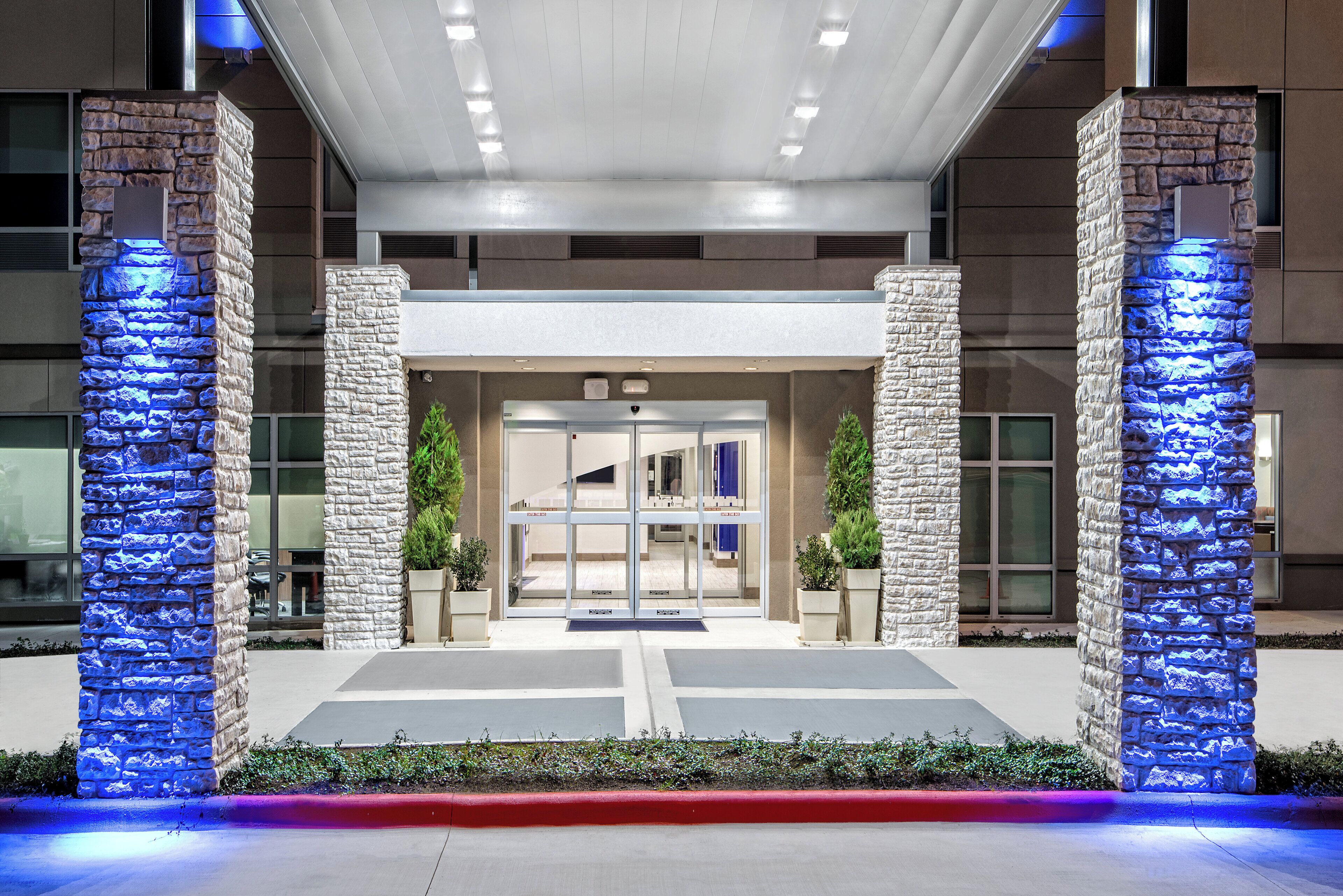 A hotel entrance with stone pillars, glass doors, and a red curb.